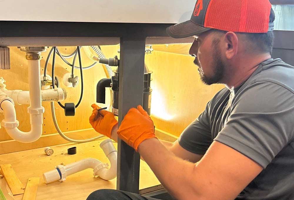 Plumber from All Hours Plumber fixing a tubular drain assembly under a kitchen sink