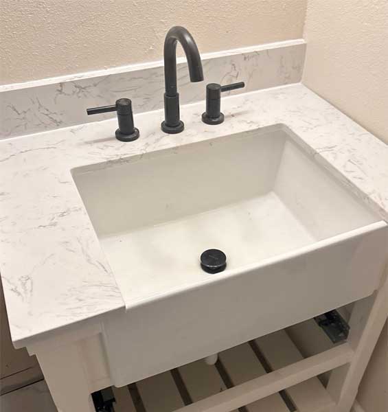 Black lavatory faucet installed on a white marble top vanity.