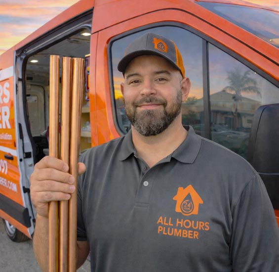 Plumber from All Hours Plumber standing in front of an open service van holding 3 copper pipes for a commercial leak repair in South Tampa