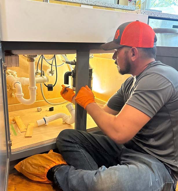 Plumber from All Hours Plumber fixing a tubular drain assembly under a kitchen sink