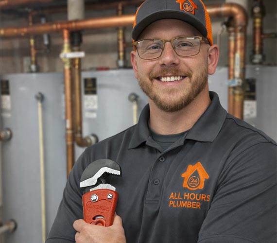 James from All Hours Plumber standing in front of commercial water heater bank holding a pipe wrench.